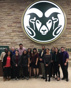 The members of the PMSAC stand together in front of a large ram head logo